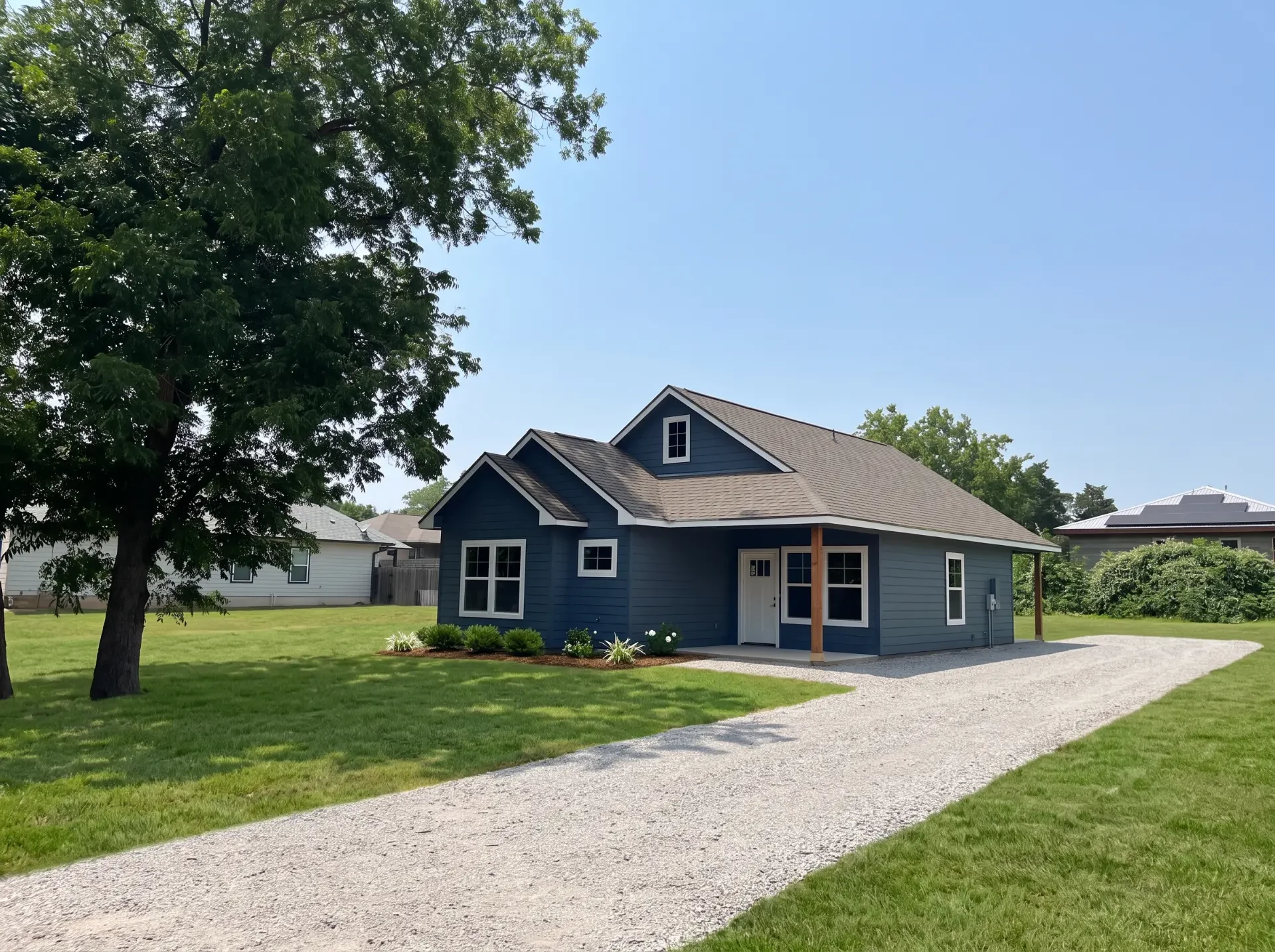 Blue single-story home with covered porch, gravel drive and mature shade tree